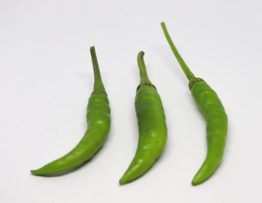 Bu yakın çekim taze ve mutfak malzemelerini vurgulayarak, el değmemiş beyaz bir zemin üzerinde sapları olan üç canlı yeşil kırmızı biberi vurgular..