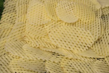 Resimde çok sayıda waffle kesimi patates dilimleri, çapraz desenleri dokulu ve görsel olarak çekici bir yüzey oluşturur. Işık, her bir çipin karmaşık detaylarını yakalar..
