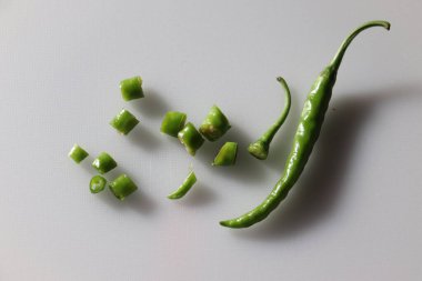 Doğranmış kısımların yanında tek bir yeşil biberli biber içeren bu fotoğraf, temiz ve beyaz bir yüzey üzerindeki biber hazırlıklarına canlı bir bakış sağlar..