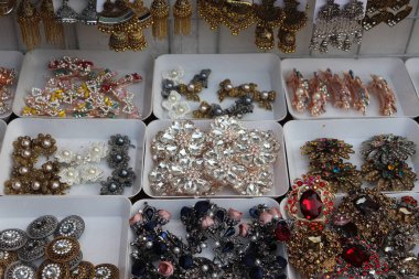 Yüksek açı, bir dükkanda çeşitli parıltılı aksesuarlarla dolu tepsileri yakalar; mücevher tipleri mücevher broşlarından mücevher tokalarına, çiçek tokalarına kadar pek çok tarz seçeneği sunar.