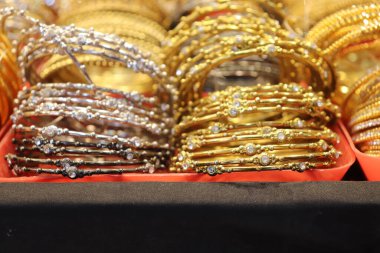 Yakından bakınca, her biri pırıl pırıl kristallerle süslenmiş güzel bir altın ve gümüş bilezik koleksiyonu ortaya çıkıyor, güzelce sergileniyor ve satılık kırmızı bir yüzey üzerinde sunuluyor..