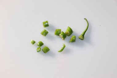 Beyaz bir yüzeye saçılmış birden fazla yeşil biber kesiği, doğal bir canlı besin bileşeni olan bir tutam baharat ekleyerek ortaya çıkar..