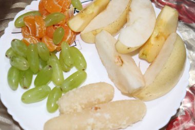 Gösterişli vitrinler, dilimlenmiş armutlar, yeşil üzümler, beyaz bir tabakta soyulmuş portakal parçaları, renkli ve sağlıklı bir meyve çeşitliliği sunar..