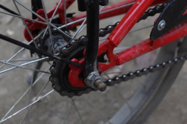 Kırmızı bisiklet çerçeve ve arka tekerlek yakın çekim, zincir ve dişliler ile karmaşık mekanik vurgulama, ayrıntılı bir görünüm sağlar.