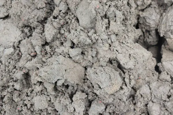 Gri toprak yığınının yakın görüntüsünde pürüzlü ve pürüzlü bir doku var. Sıkıştırılmış toprak, daha küçük parçalara ayrıldığını gösteriyor..