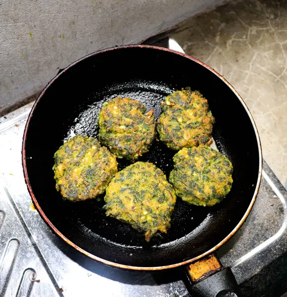 Yukarıdan aşağı beş ıspanaklı kekin gaz sobasında siyah bir demir tavada pişirildiğini gösteriyor, eski bir duvar yüzeyinin arka planına kurulmuş..