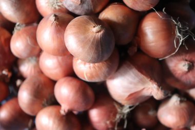 Yakın plan çekimde bir yığın taze kırmızı soğan ve parlak derileri ışığı yansıtıyor. Ampul yığını yoğun, organik bir doku oluşturur. Mutfak veya gıda projeleri için idealdir..