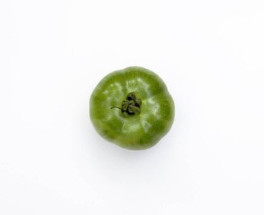 Olgunlaşmamış yeşil bir domatesin canlı dokusunu yakalıyorum. Görüntü, bu renkli meyvenin organik güzelliğini ve tazeliğini temiz, beyaz bir zemine karşı gösteriyor..