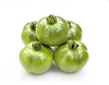 Bir piramit oluşturmak için istiflenmiş beş olgunlaşmamış yeşil domatesi kapatın. Pürüzsüz, parlak bir teni var ve yeşil renk ona yeni bir görünüm veriyor. Çekim beyaz arka planda..