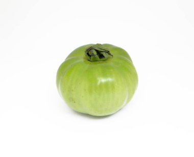 Yakın çekim pürüzsüz dokuyu ve olgunlaşmamış domatesin eşsiz şeklini vurguluyor. Canlı yeşil rengi, saf beyaz zemin ile zıtlaşır ve tazeliğini vurgular..