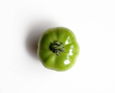 Tek, pürüzsüz, yeşil domatesin gövdesi bozulmamış, taze ve canlı özelliklerini vurgulayan beyaz bir arka plan üzerine kuruludur..