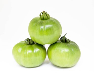 Bu canlı natürmort yaşam, birbirine üst üste istiflenmiş üç olgunlaşmamış yeşil domatesin beyaz arka plana karşı bir canlılık ve doğal potansiyel göstergesi..