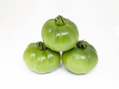 Yeni toplanmış, hafifçe parlak, piramit şeklinde dizilmiş üç yeşil aile yadigarı domates temiz, minimalist beyaz arka plana karşı, canlı renklerini ve dokularını vurgulayarak,.