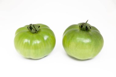 Canlı görüntü iki olgunlaşmamış yeşil aile yadigarı domatesleri, eşsiz şekillerini ve dokularını sergileyerek, saf beyaz bir arka planda yan yana gösteriyor. Doğal ürünlere odaklan.