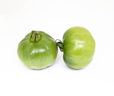 Görüntü bir çift olgunlaşmamış domatesin yan yana olduğunu gösteriyor, sapları hala bağlı, bu da tazeliği gösteriyor. Domateslerin pürüzsüz, yeşil teni saf beyaz arkaplan ile güzel bir tezat oluşturuyor..