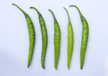 Beş taze, uzun, çiğ, yeşil kırmızı biber düzgün beyaz bir arkaplan üzerine dizilmiş, doğal renklerini ve şekillerini sergiliyorlar..