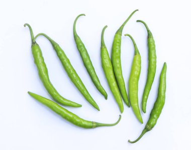 İnce yeşil kırmızı biber dizisi, canlı yeşil sapları ile organik olarak dağınık, beyaz bir zemin üzerinde, onların dokusu ve renk çeşitliliği vurgulanıyor.