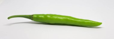 Temiz ve beyaz bir arkaplanda tek bir olgunlaşmamış kırmızı biber sergilenir. Biber, sapından ucuna kadar pürüzsüz bir doku ve düzgün yeşil renk sergiler..
