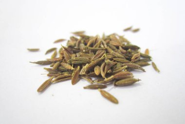 Dağınık kahverengi kimyon tohumları beyaz bir yüzeyde duruyor.