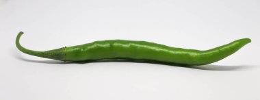 Bu büyüleyici çekim, pürüzsüz, ince desenli yüzeyi olan, el değmemiş beyaz bir arkaplana yatay olarak uzanan uzun, canlı yeşil bir kırmızı biberi içeriyor. Kavisli kökü karakter ekler.