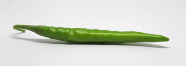 Bu yakın plan tek bir parlak yeşil kırmızı biberi yatay olarak dinlenirken gösteriyor. Biberin pürüzsüz cildi ışığı yakalar ve kökü hafifçe yana doğru kıvrılır..