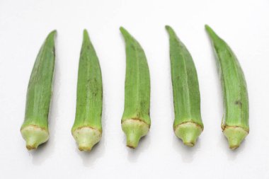 Beş ayrı, taze bamya kabuğu açık beyaz bir zemine karşı canlı yeşil bir renk sergiliyor. Sivri uçlu ve desenli yüzeyleri açıkça görülüyor. Bu da son zamanlarda hasat yapıldığını gösteriyor..