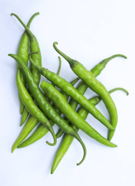 Tepeden çekimde beyaz bir düzlemde birbirine karışmış birkaç yeşil biber görülüyor. Biberler taze yeşil renkler sergiliyor, doğal ve canlı bir estetiğe katkı sağlıyor..