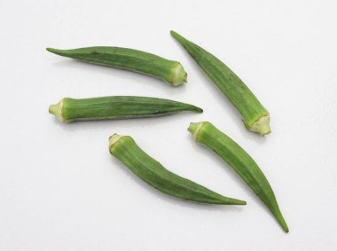 Yukarıdan aşağıya doğru beş taze, yeşil bamya kabuğu saf beyaz bir zemin üzerinde doğal dokularını ve renklerini vurgulayarak zarif bir şekilde yerleştirilmiş..