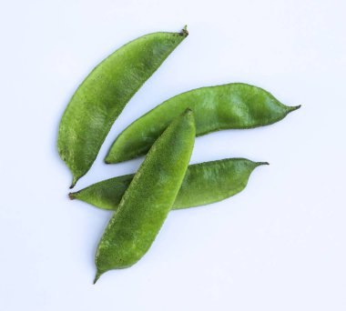 Taze toplanmış yeşil lima fasulyeleri açık, beyaz bir zeminde sergileniyor, renkleri ve dokuları vurgulanıyor. Doğal ışık, görüntünün görsel çekiciliğini arttırır..