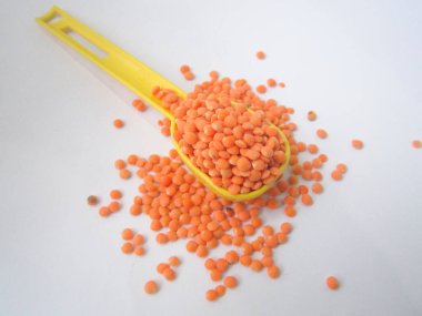 Kırmızı mercimeği bol bol doldurur parlak sarı bir plastik kaşığı beyaz bir zemine karşı