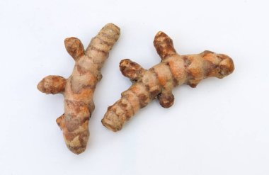 Yakından çekilen iki ham zerdeçal, pürüzlü, pürüzlü dokularını ve parlak turuncu rengini katıksız beyaz arka planda sunar. Kafiyeler izole bir şekilde oturur, doğal hallerine dikkat çekerler..