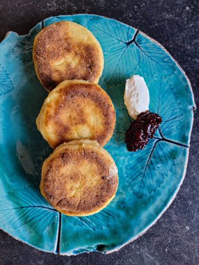 Güzel bir mavi tabakta, ekşi krema ve vişne reçelli Ukrayna peynirli kek Syrniki. Geleneksel Ukrayna mutfağı yemeği