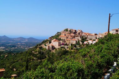 Akdeniz 'e karşı Speloncato köyü manzarası, mavi gökyüzü, güneşli bir günde yeşil vadi ve dağlar. Balagne, Korsika, Fransa.
