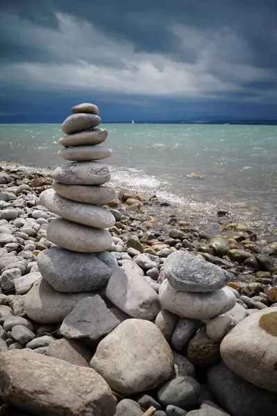 Çakıl taşı kulesi, taşlar, güneş ışınları, deniz kıyısı ya da gölde su ve dramatik gök gürültülü fırtınaya karşı. Denge, meditasyon ve dinlenme yeri.