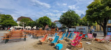 Landungsplatz, Ueberlingen, Almanya 'da halka açık alanda. 06 Temmuz 2024. Doğaçlama plaj alanı olan turuncu masa ve banklar yeşil ağaçların arka planında, bir meydanda yer almaktadır..