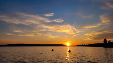 Constance Gölü 'ndeki inanılmaz gün batımı. Stand Up Paddle tahtasındaki insanların siluetleri güneş sisteminin arka planında. Su sporları.