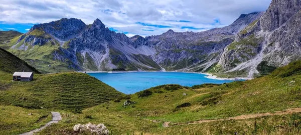 Luner Gölü Luenersee 'nin mavi sularıyla manzaralı bir panoramis manzarası. Önde yeşil tepeler ve arkada küçük bir ev var. Görkemli Alpler. Avusturya 'nın en büyük göllerinden biri..