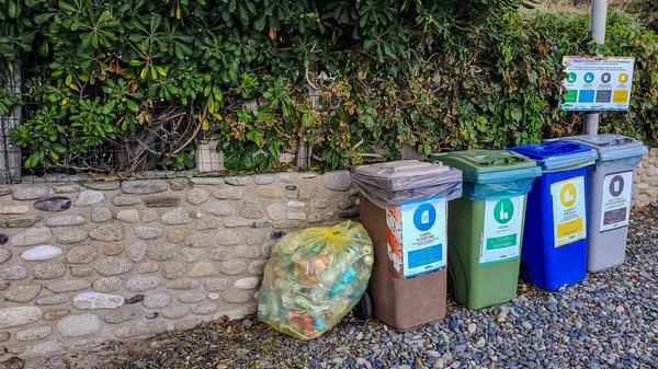 Dört renkli çöp konteynırı ve sahilde bir sarı çanta. Çevresel koruma. Farklı düşün. 21 Eylül 2024. Pomonte, Toskana Bölgesi, Elba Adası, İtalya