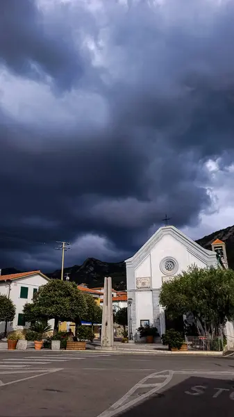 Elba, Toskana, İtalya 'daki Akdeniz kenti Pomonte' deki kilise ve Santa Lucia Meydanı. Arka planda - bir fırtına gökyüzü.