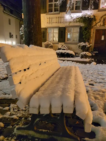 Beyaz pofuduk karla kaplı bankın akşam manzarası. Arka planda pencerelerinde ışık olan eski bir ortaçağ evi var..
