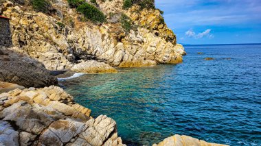 A fascinating view of a picturesque beach with clear azure water. In the foreground - textured stones, on the back - the cheekbones covered with green trees. Elba, Marciana Marina. clipart