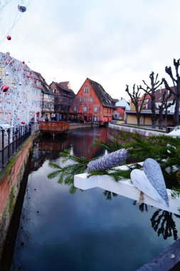 Colmar, Fransa 'da Noel. Ön planda - kalp, tümsek ve çam dalı. Arka planda - dekoratif Noel ağaçları, yarım kereste evler ve nehrin ayna yüzeyi.