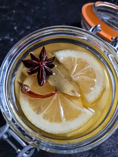 Salamurada cam kavanozdaki iştah açıcı limon dilimlerinin üst görüntüsü. Üstte anason yıldızı, kırmızı biber ve defne yaprağı.