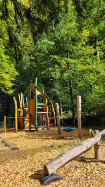 The part of playground for children made of predominantly natural materials in the green forest. Climbing castle, swing of different types and horizontal bars. clipart