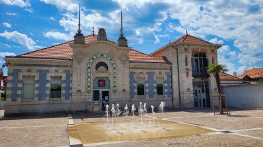 Caisse dEpargne bankasının orijinal mimari tarzına sahip çok güzel bir bina. Girişinde bir amblem var. Ön planda bir çeşme var. 11 Haziran 2022. Soulac-sur-Mer, Medoc, Yeni Aquitaine, Fransa.