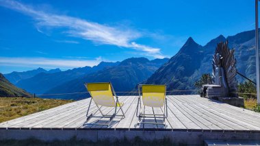 Turistler için Ischgl, Tyrol, Avusturya 'da inanılmaz güzel dağ manzaralarının tadını çıkaran iki rahat sarı sandalye.