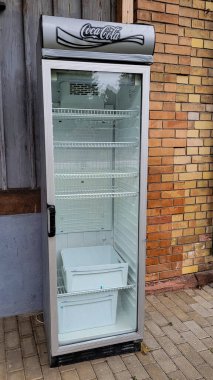 Cam kapılı boş bir buzdolabı ve dışarıda duran Coca-Cola logosu. Boş vaatler. Önce Amerika. 12 Aralık 2024. Uberlingen, Nussdorf, Almanya.