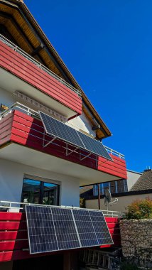 İki balkon güneş sistemi, beyaz bir apartmanın kırmızı balkonunda 30 ve 20 derecelik açıyla sabit. Almanya 'da konut teknolojisi.