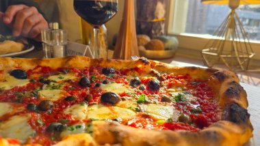 Domates soslu iştah açıcı pizza, zeytin, ançüez, peynir ve kapari, dilimlenmiş. Arka planda bir kadeh kırmızı şarap var..