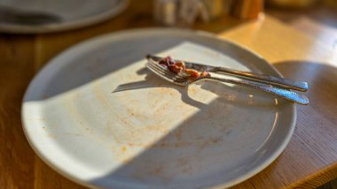 Lezzetli bir öğle yemeğinden ya da zeytin, çatal ve bıçaklı bir yemekten sonra ahşap bir masada boş ve kirli bir pizza tabağı. Seçici odak.